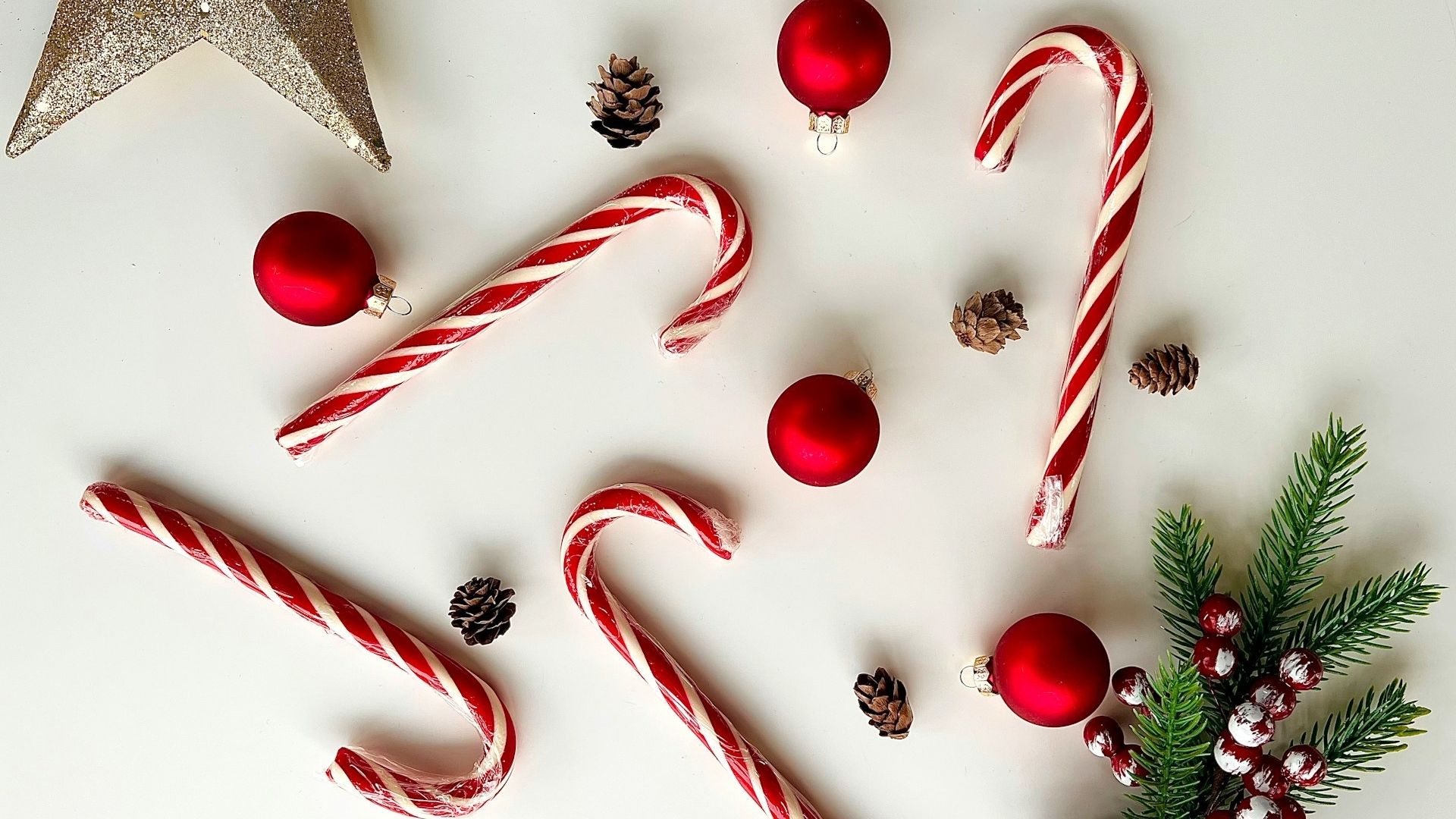Bastones de caramelo rojos y blancos junto a bolas, piñas y ramas navideñas
