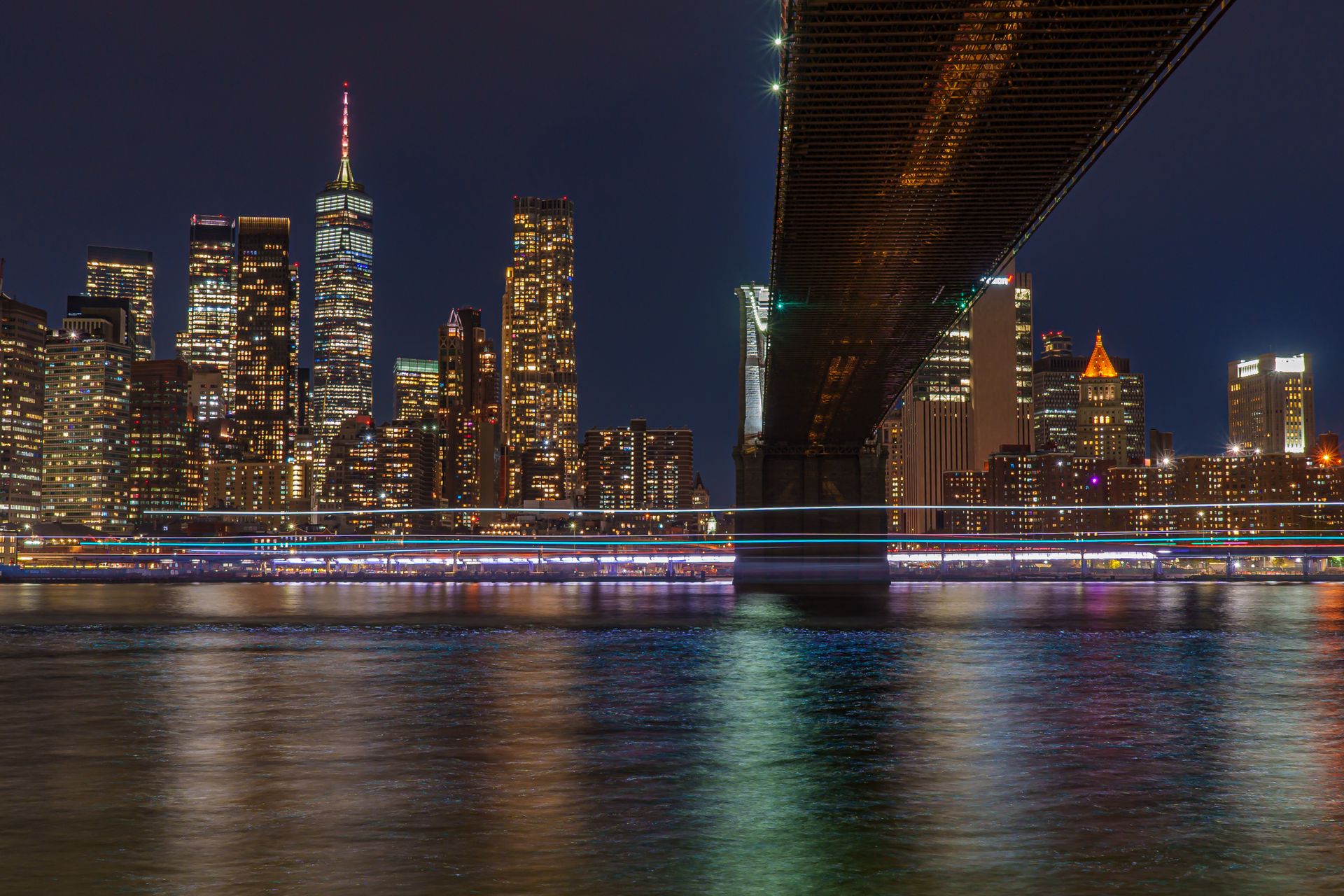 Skyline nocturno de Nueva York junto al río y bajo un puente