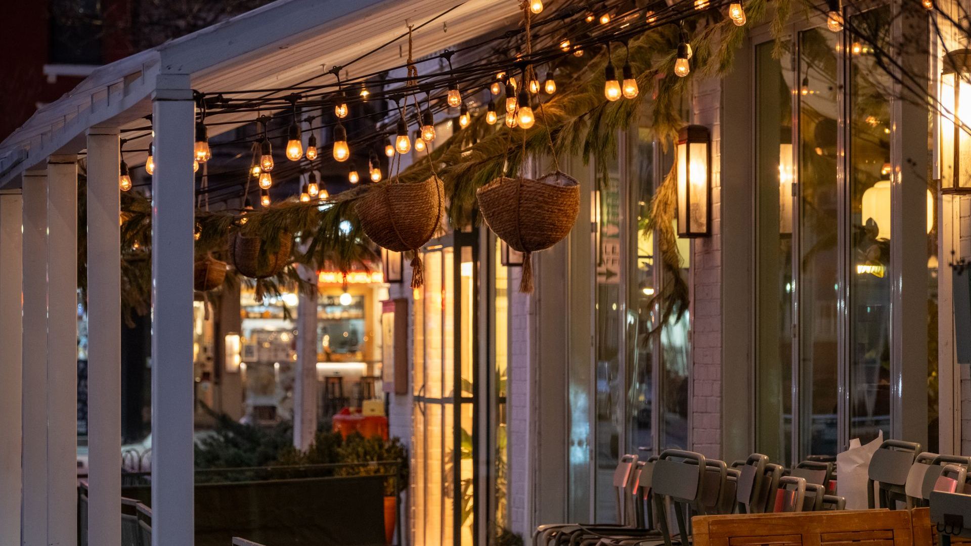 Terraza de restaurante con mesas, plantas y una guirnalda de bombillas.